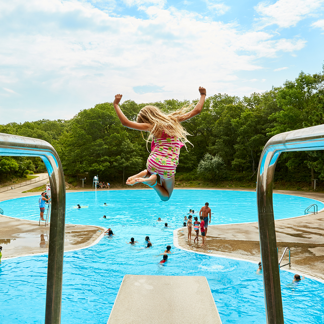 Girl jumping off diving board into pool