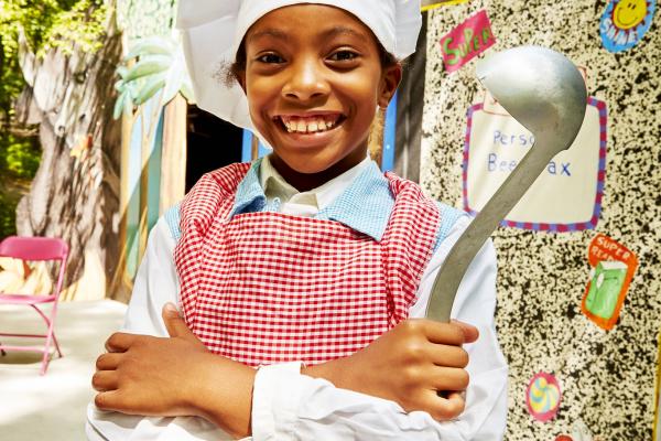 Young smiling girl dressed in a chef's costume and holding a ladle