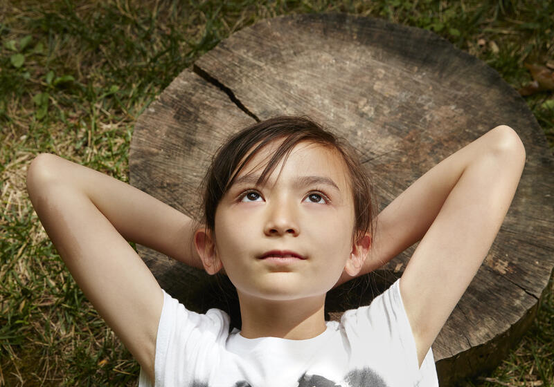 Young girl lying on a log with her hands behind her head.