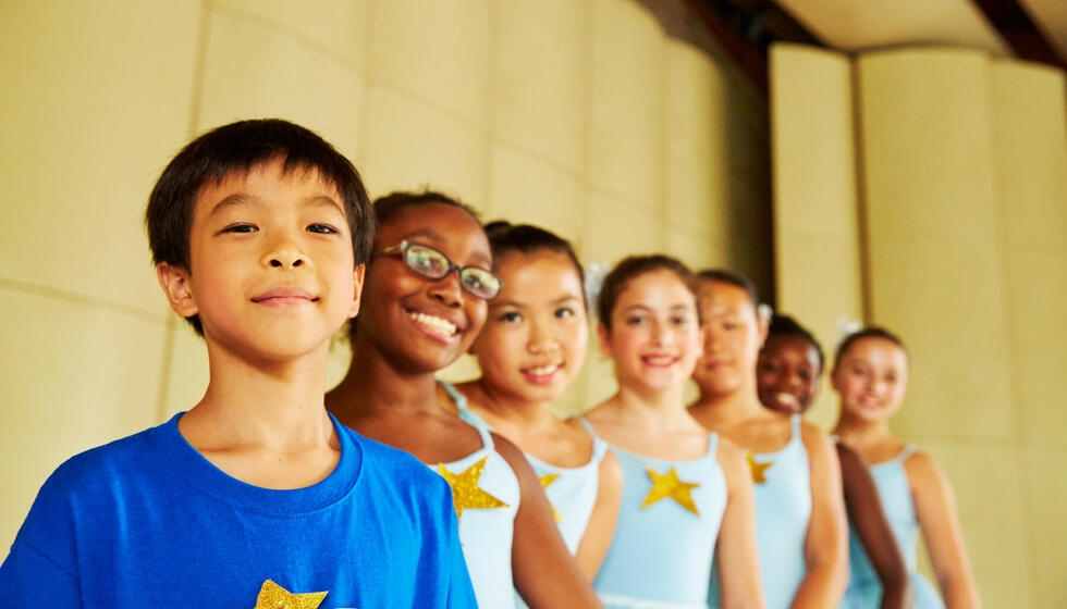 Seven kids in blue and white ballet costumes posing on stage