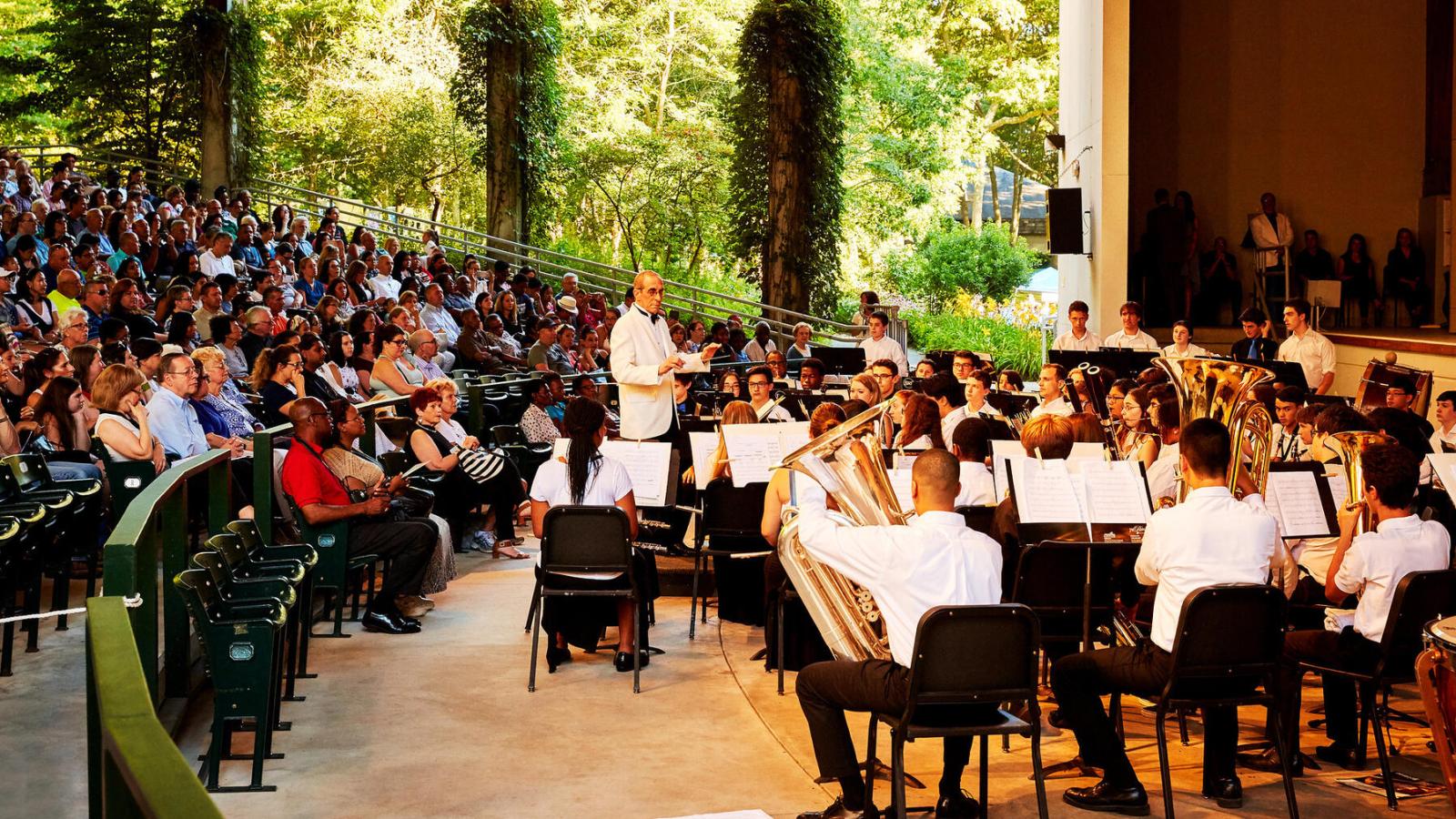Conductor in front of band in Amphitheater surrounded by green nature