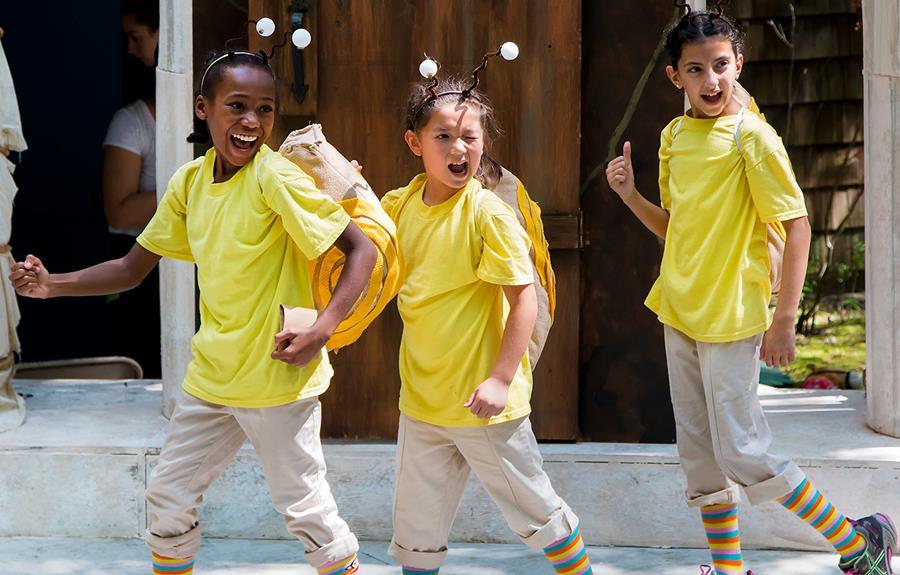 Three young actors in bee costumes, winking at the audience