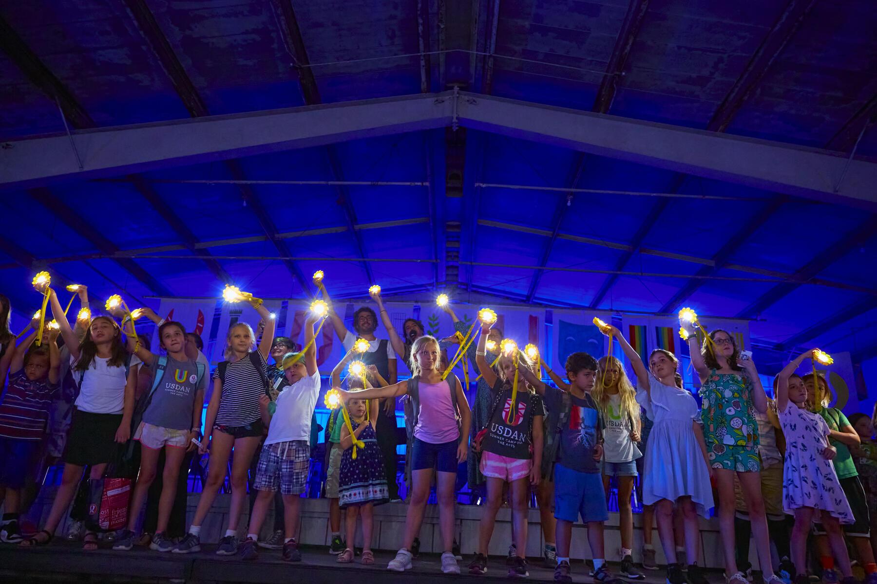 Children standing on stage holding lights and waving them in the air 