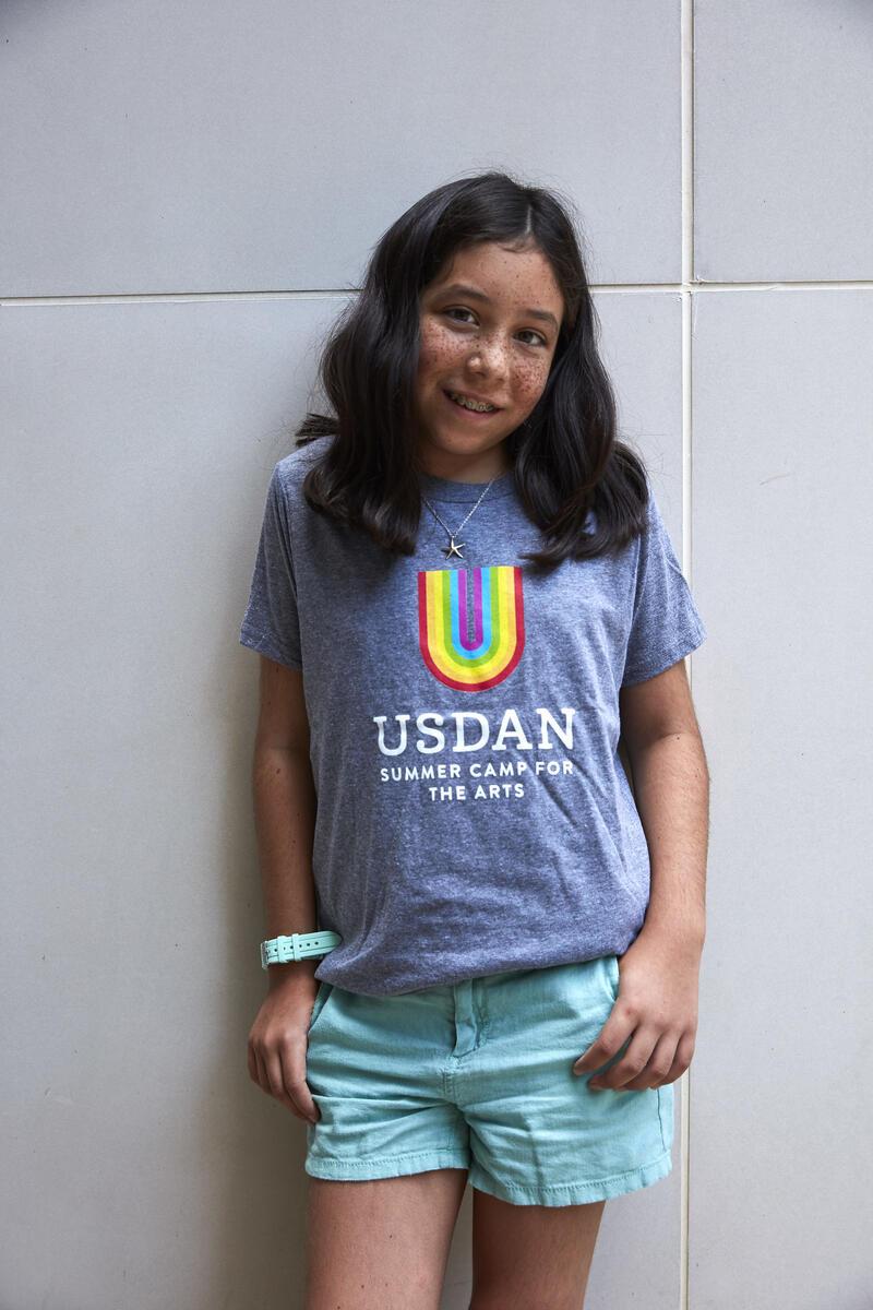 Young girl standing in Usdan t-shirt with rainbow U 