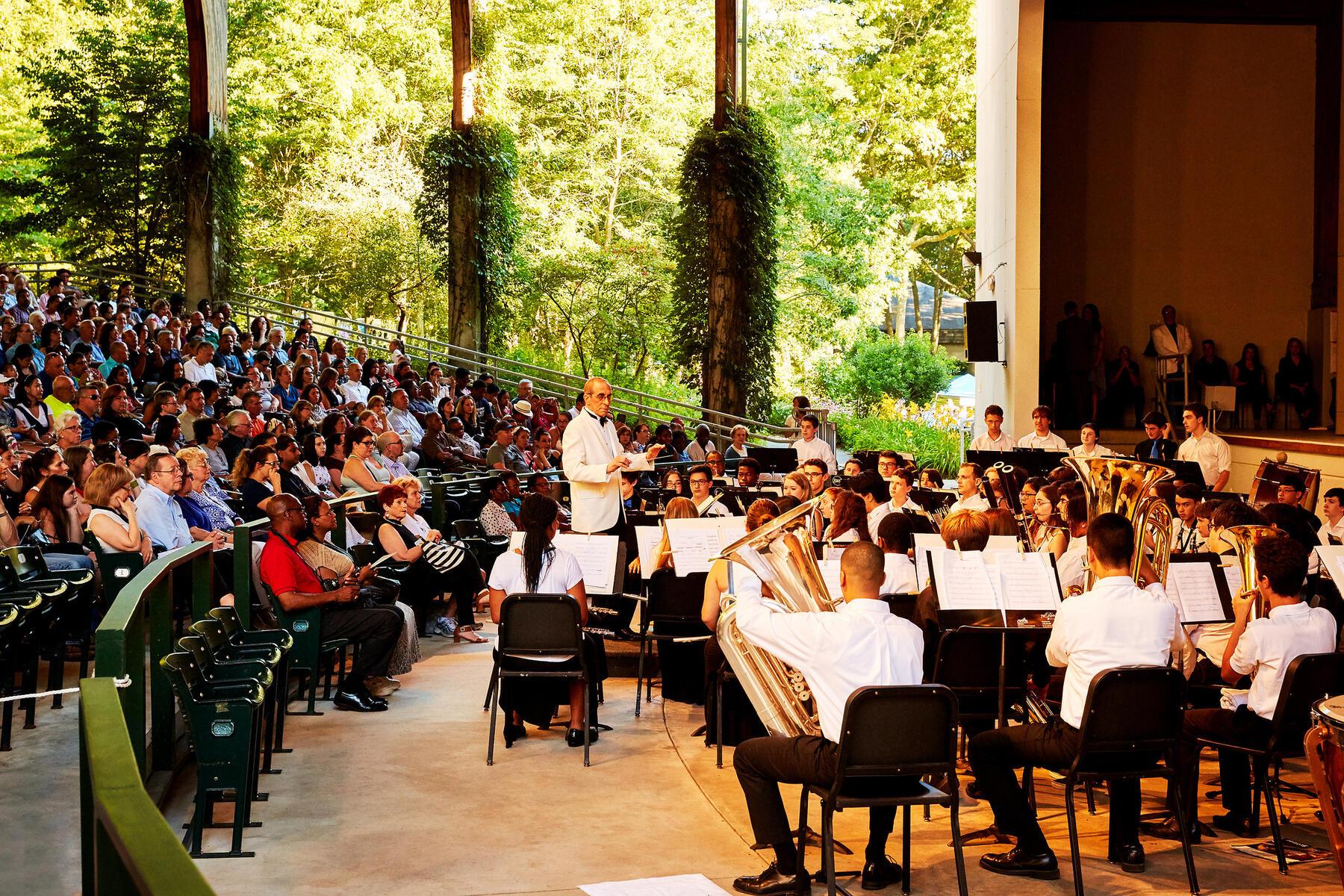 Conductor in front of band in Amphitheater surrounded by green nature