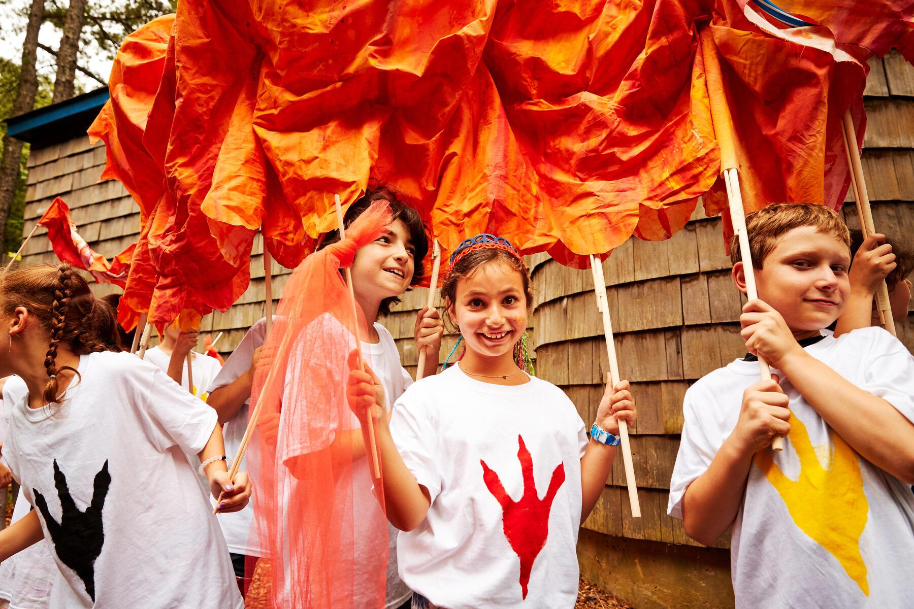 Group of children holding poles to a large puppet and looking at the camera