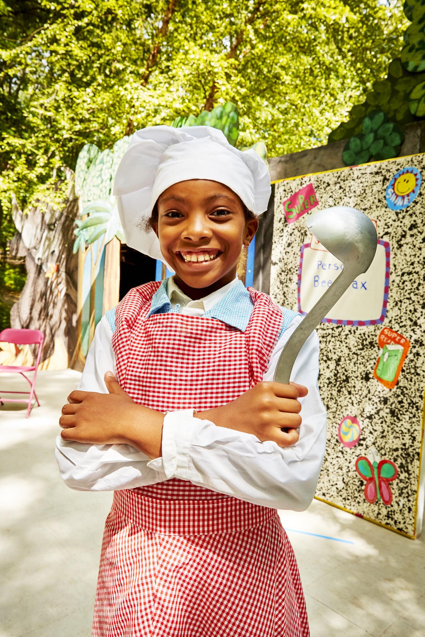 Young smiling girl dressed in a chef's costume and holding a ladle