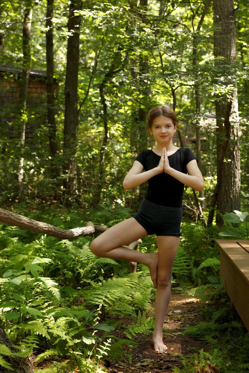 Young girl striking the Yoga Tree pose in the woods