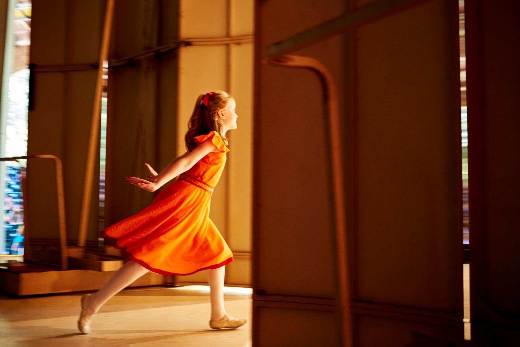 A young dancer in an orange dress running onto the Amphitheater stage