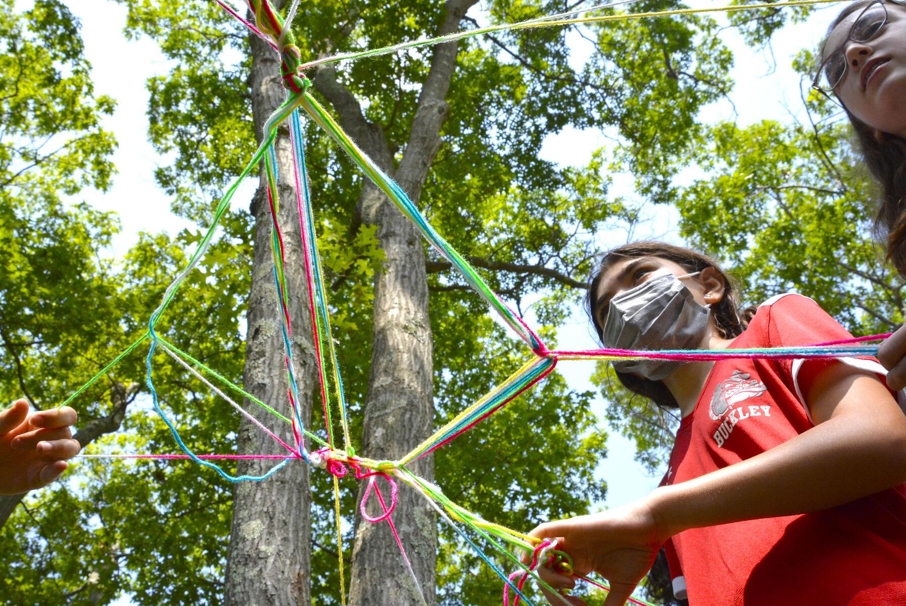 Students standing under yarn sculpture