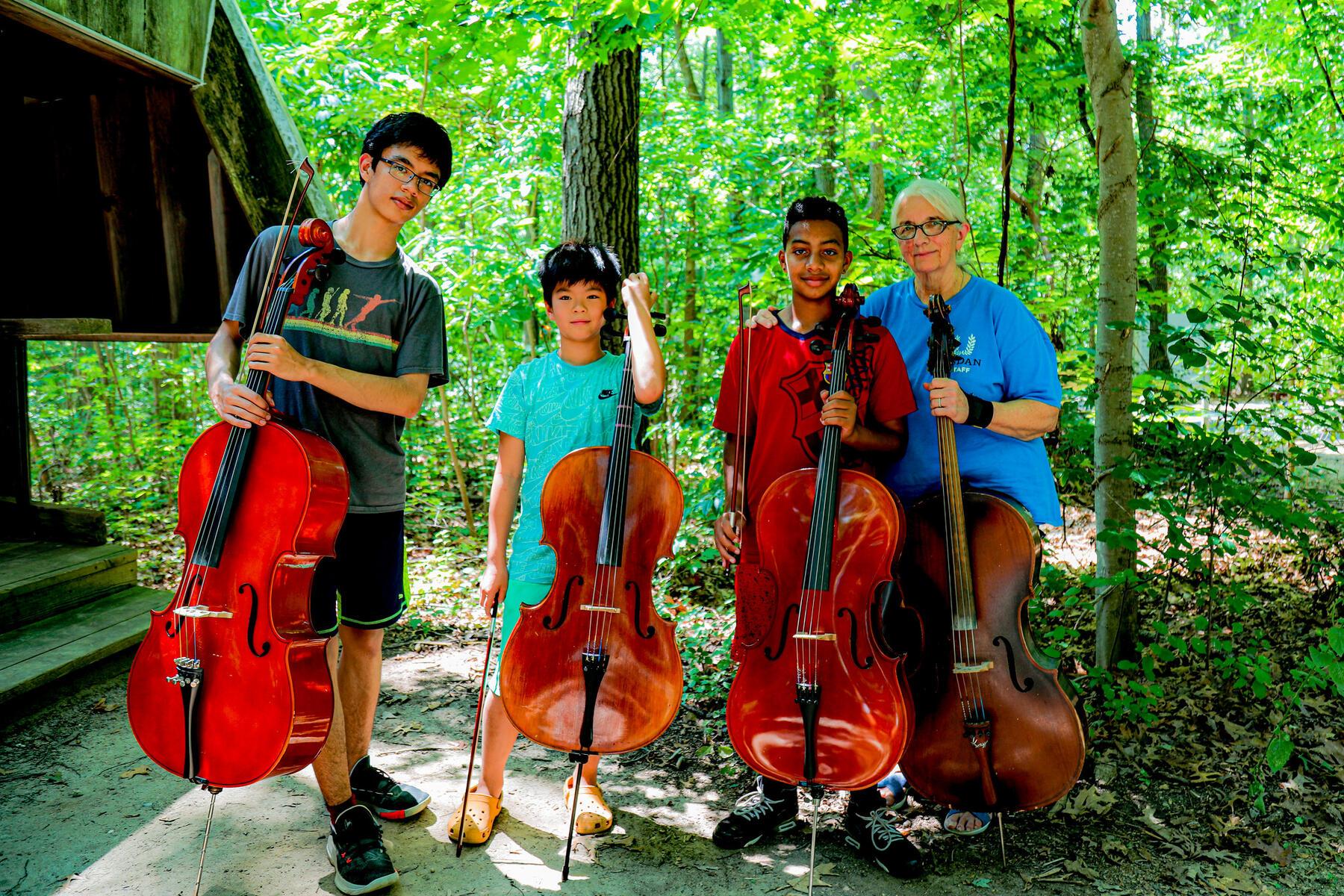 Cellists posing with their cellos in the woods