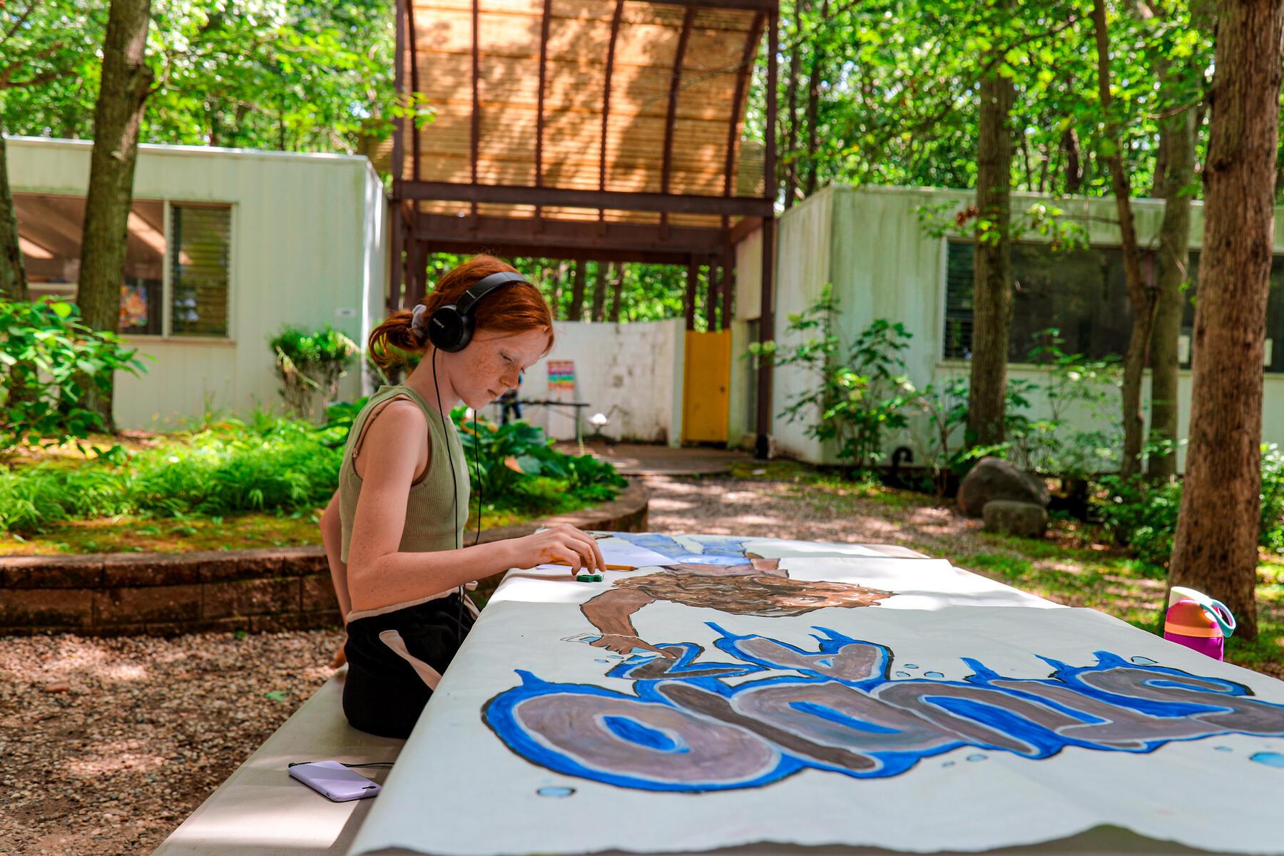 Student sitting in the woods painting and listening to music