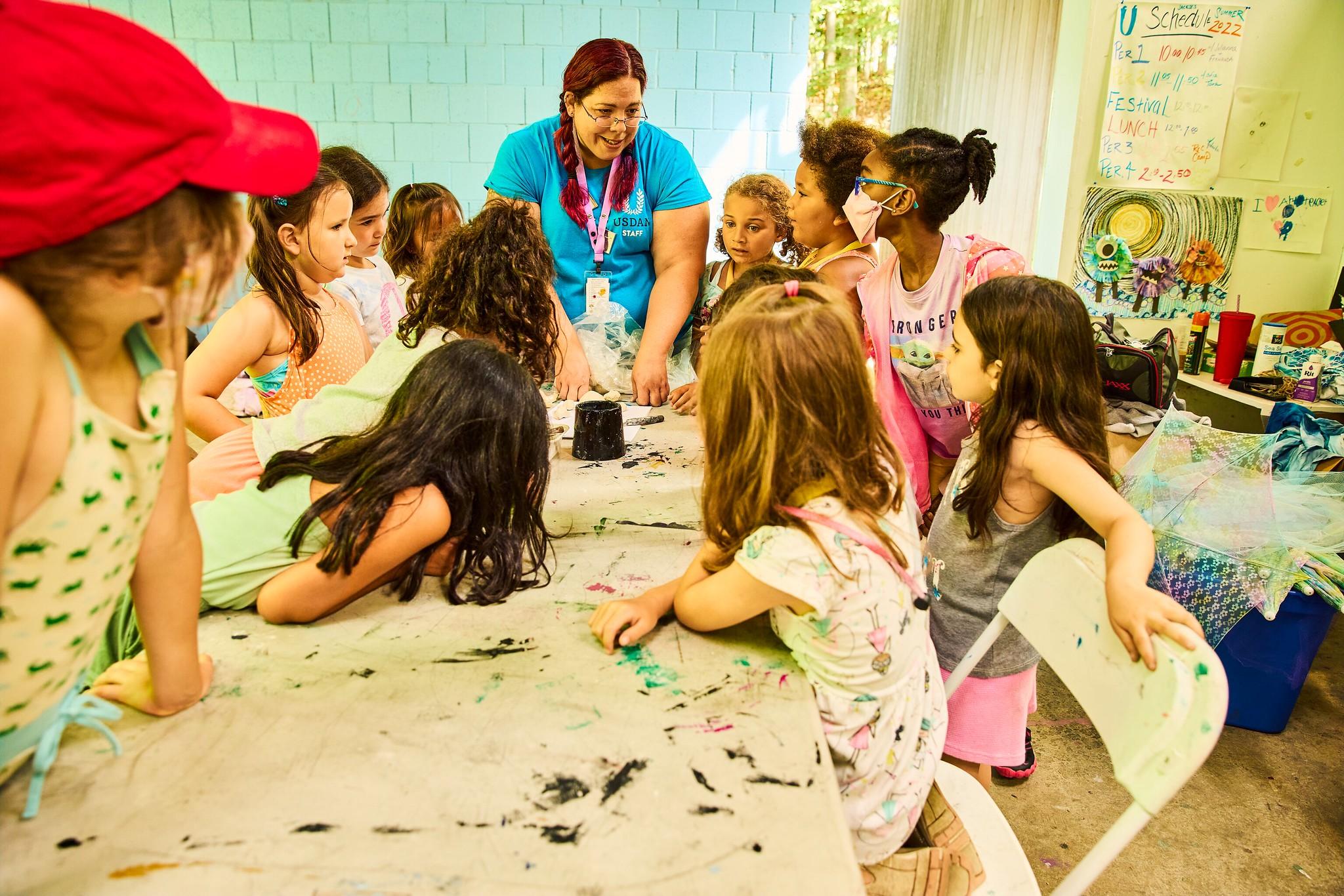 Students standing around an art table listening to their teacher