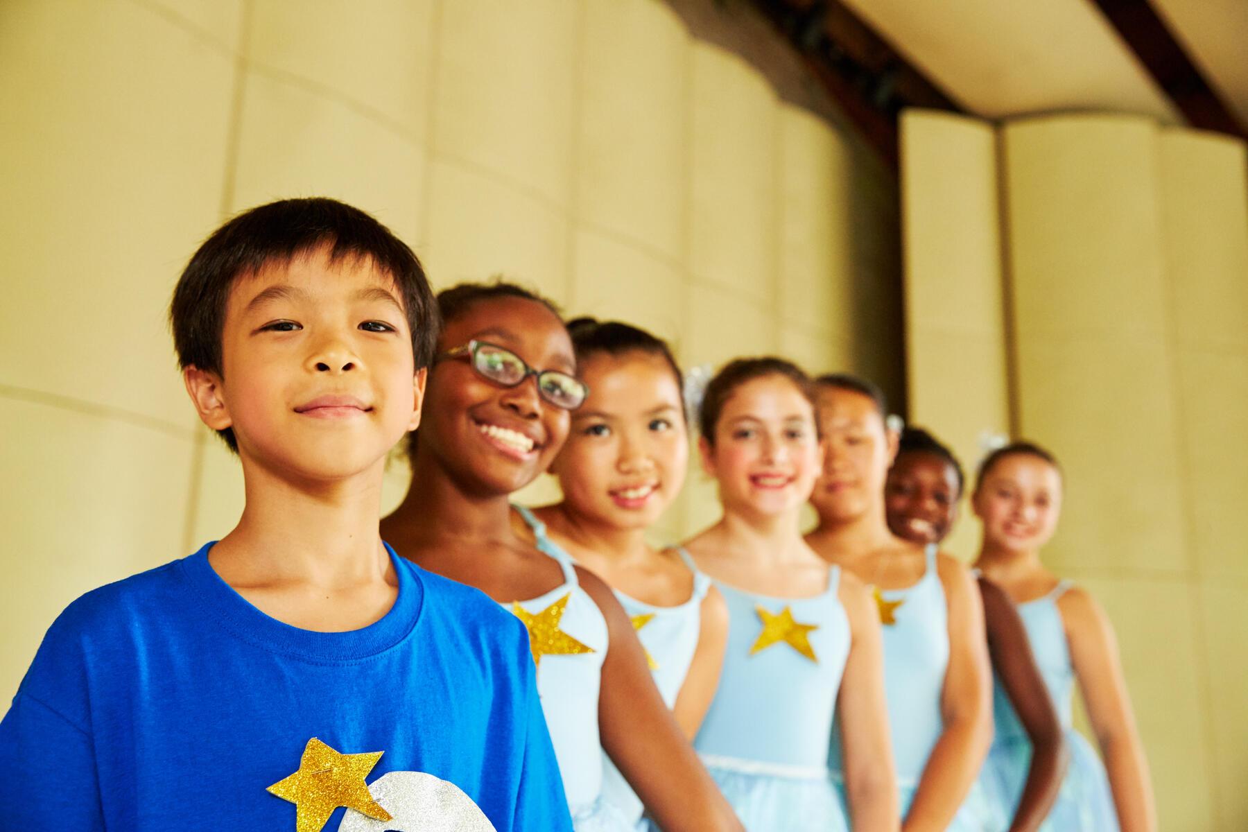 Seven kids in blue and white ballet costumes posing on stage