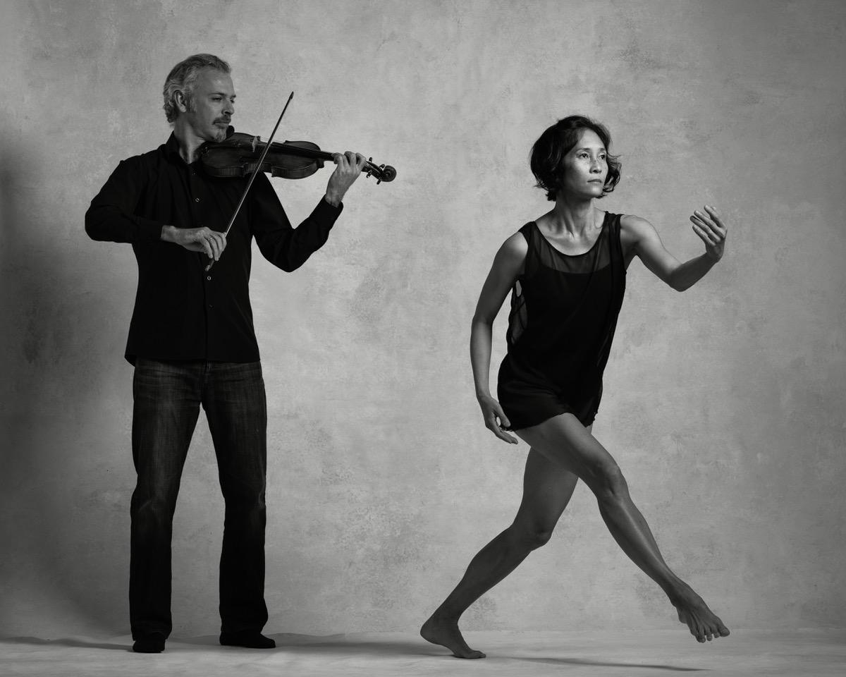 Black and white photo of Colin Jacobsen emotionally playing the violin and Maile Okamura mid-movement