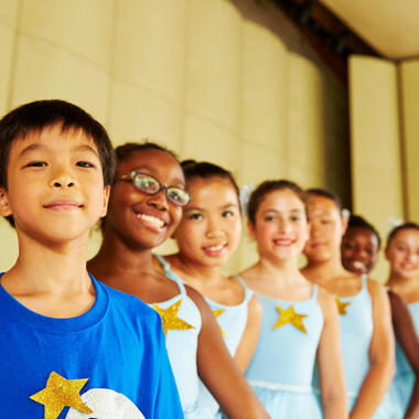 Seven kids in blue and white ballet costumes posing on stage