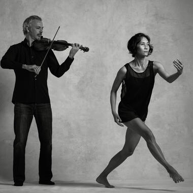 Black and white photo of Colin Jacobsen emotionally playing the violin and Maile Okamura mid-movement.